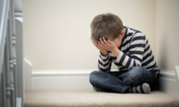 A child in a striped jumper sitting cross-legged on the floor with his head in his hands