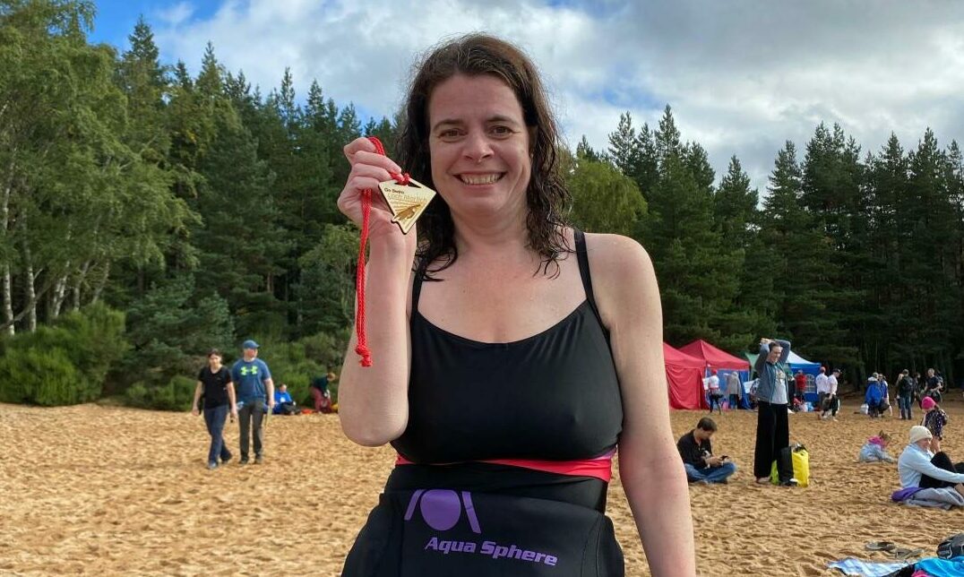 Nicola after her swim, holding a medal on the banks of Loch Morlich.