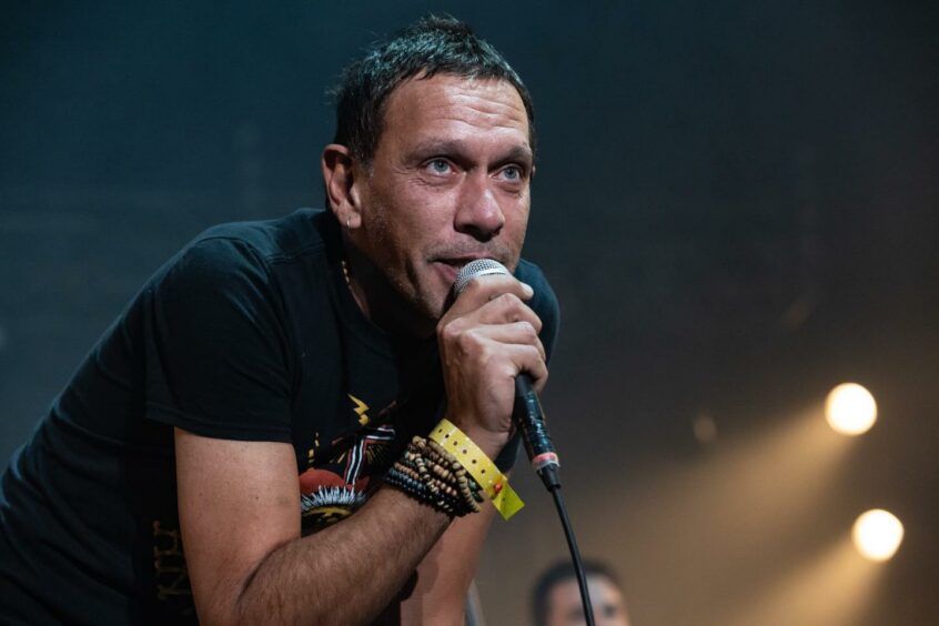 Shed Seven lead singer Rick Witter holding a microphone while performing at the 2021 Isle of Wight Festival.