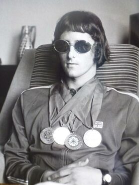 Jim Muirhead wearing a tracksuit and dark glasses with four medals around his neck.