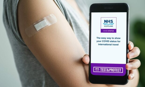 Someone with a plaster on their arm holds up the NHS Covid Scotland passport app.