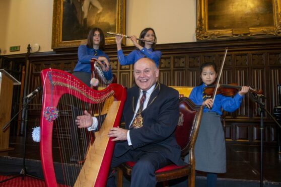 The Lord Provost sits at a harp with ST Margaret's musicians behind him