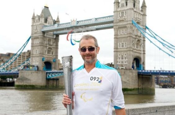 Holding a silver olympic torch in front of Tower Bridge is Jim Muirhead. 