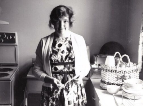 Standing in her kitchen looking at the camera is Maureen Kneen.