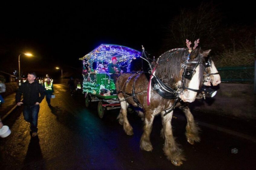 The Balmalcolm Clydesdales at Christmas, pulling a carriage covered in Christmas lights.