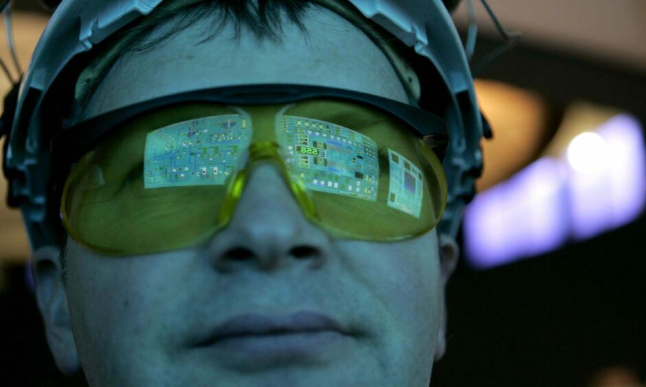 An employee works in the main control room, the console reflected in his glasses.