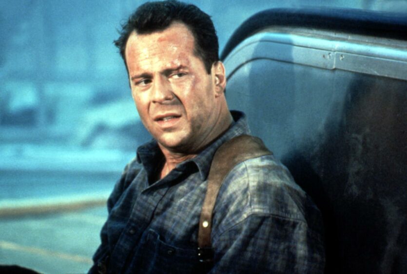 Bruce Willis in a scene from Die Hard 2, wearing the shirt that is perhaps a nod to the Scottish ancestry of John McClane.