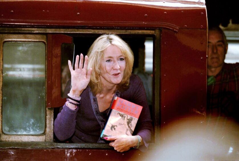 JK Rowling waving out of a window with a book