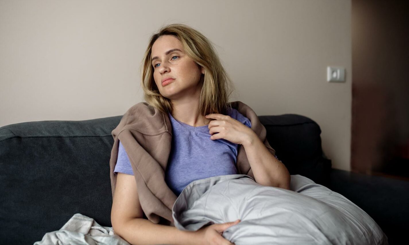 A woman with long Covid sits on a sofa,, covered in a blanket