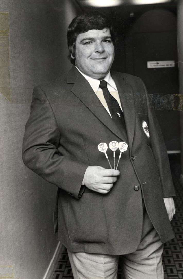 Jocky Wilson, wearing a blazer and holding up three darts
