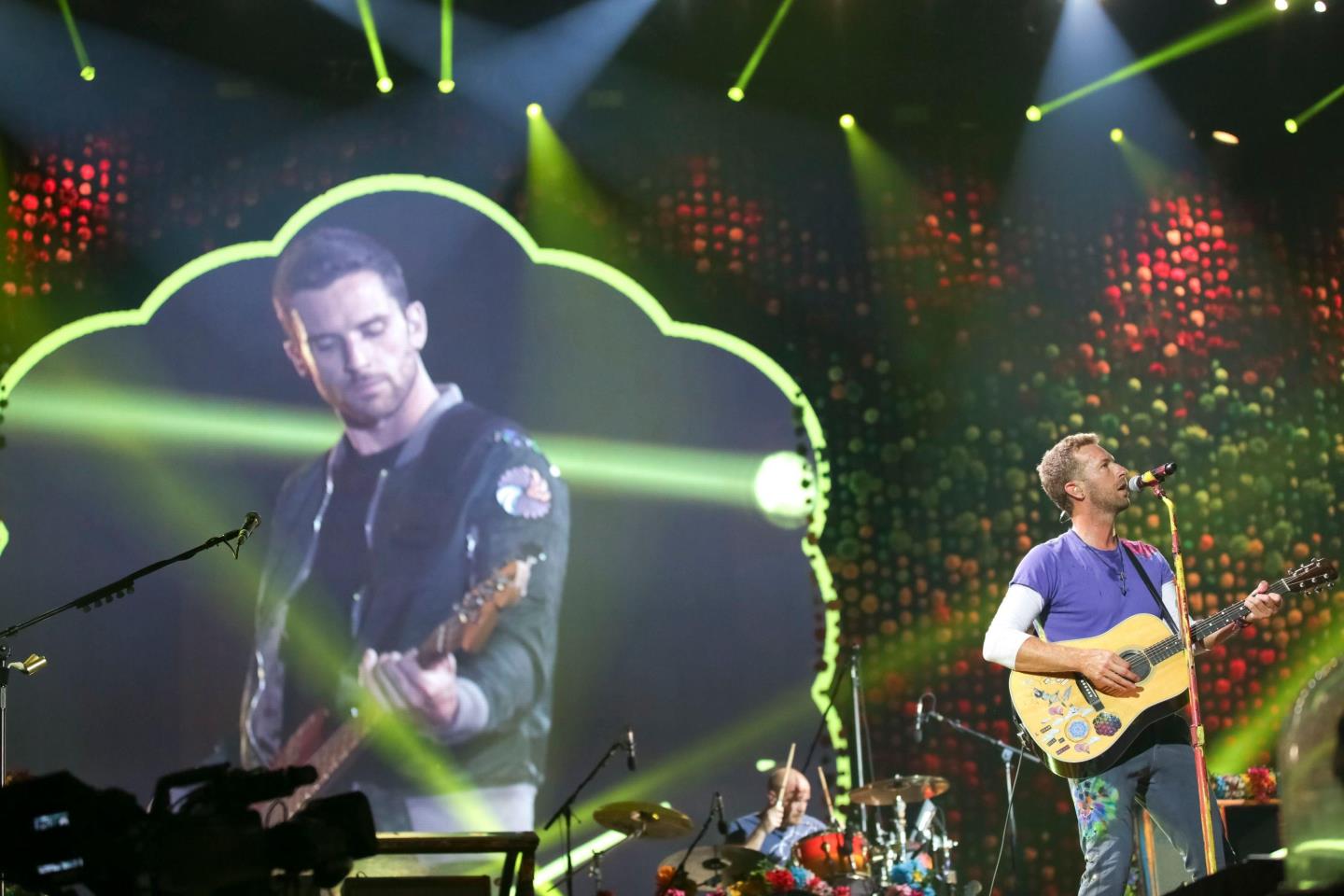 Guy Berryman's image is projected on stage behind lead singer Chris Martin during a concert in 2017.