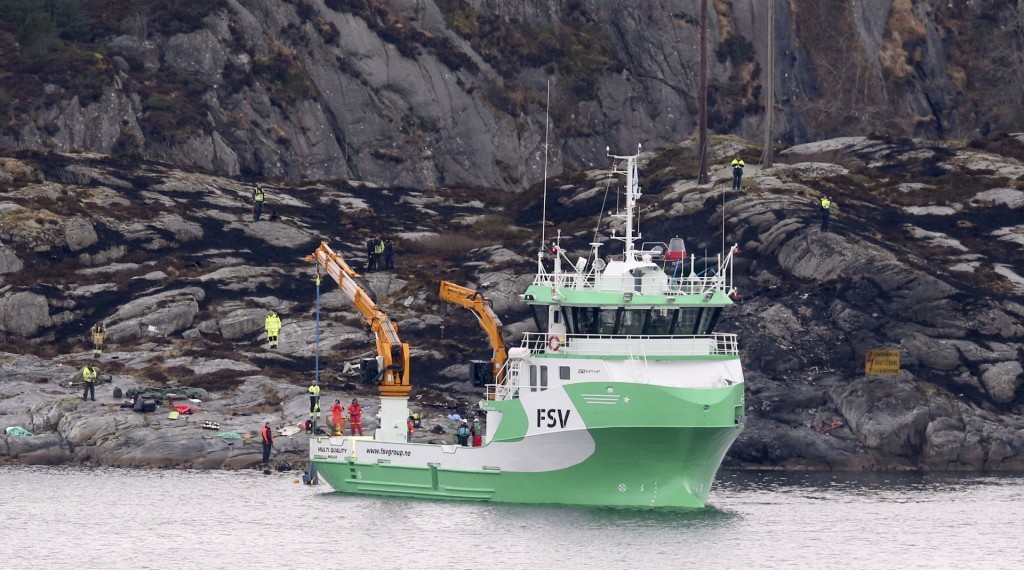 A recovery vessel lifts up parts of a crashed helicopter from off the island of Turoey, near Bergen, Norway, as emergency workers on the shoreline attend the scene Friday, April 29, 2016. The helicopter carrying around 13 people from an offshore oil field crashed Friday near the western Norwegian city of Bergen, police said. All aboard the helicopter were killed. (Vidar Ruud/NTB scanpix via AP) NORWAY OUT