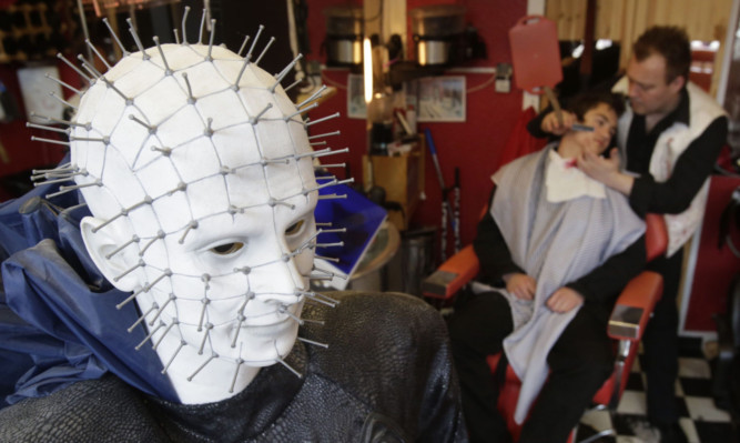 Will Robertson shaving his son Benn at his Sweeney Todd Demon Barber-themed barber shop in Pitlochry, as Pinhead watches on.