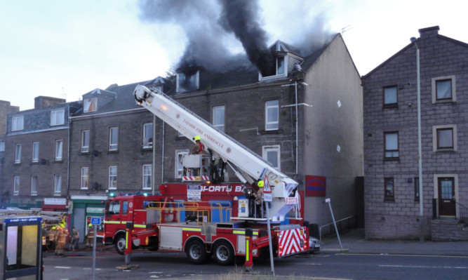 Firefighters tackling the blaze, while Simpson crouches to the right of the right-hand dormer window.
