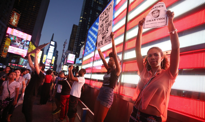 Protesters stand in front of a lit American flag in Times Square after marching from a rally for Trayvon Martin in Union Square in Manhattan.