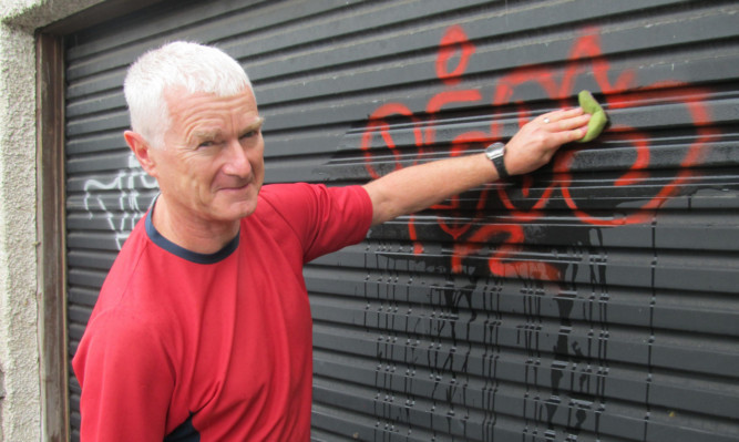 Martin Squibbs washing paint off a garage door at Blackness Road.