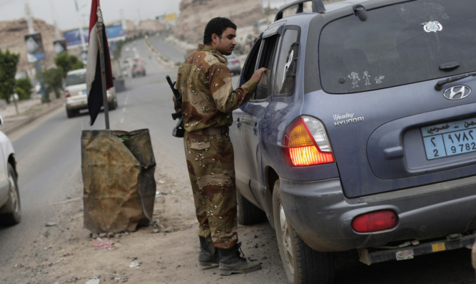 A Yemeni soldier stops a car at a checkpoint.