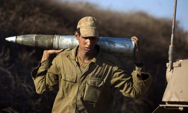 GOLAN HEIGHTS, UNSPECIFIED - AUGUST 28:  (ISRAEL OUT) A soldiers carries a shell as Israeli troops start preparations at a deployment area during a military exercise on August 28, 2013 near the border with Syria, in the Israeli-annexed Golan Heights. Tension is rising in Israel amid talks of an international military intervention In Syria following reported chemical weapons attacks. (Photo by Uriel Sinai/Getty Images)