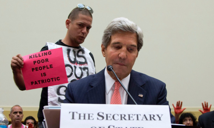 A protester makes his message heard as US secretary of state, John Kerry, addresses the House foreign affairs committee hearing on Syria.