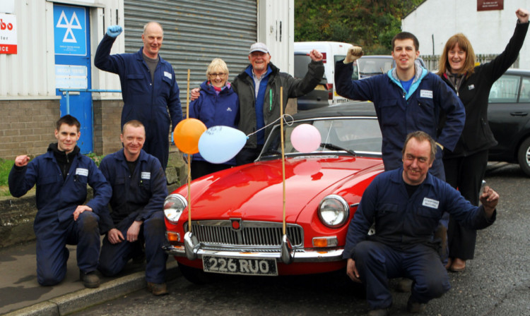 Stewart McKiddie and wife Maureen with Keith Stanford, garage staff and the MGB Roadster.