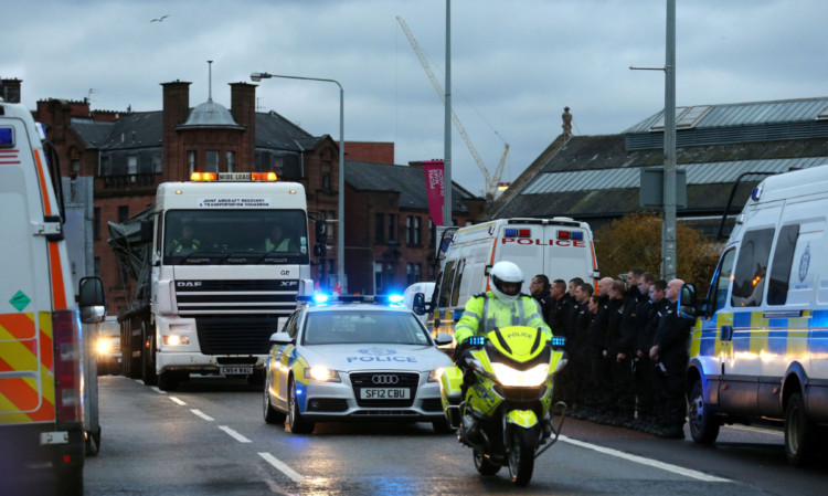Police officers line the street as the wreckage of the police three-tonne Eurocopter is taken away by lorry after being lifted from the Clutha Vaults pub.