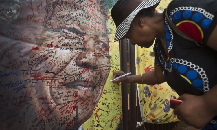 A well-wisher writes a message of condolence on a poster of Nelson Mandela outside his former house in Soweto.