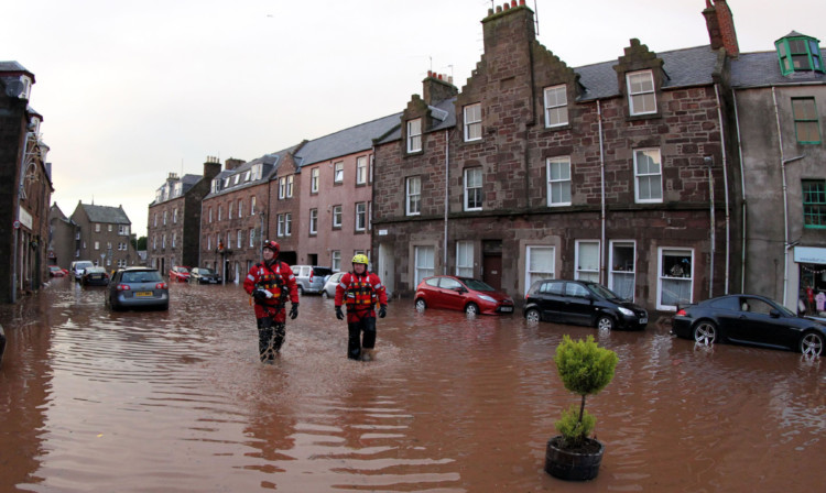 Firemen walking through floodwater on High Street in Stonehaven after heavy flooding.