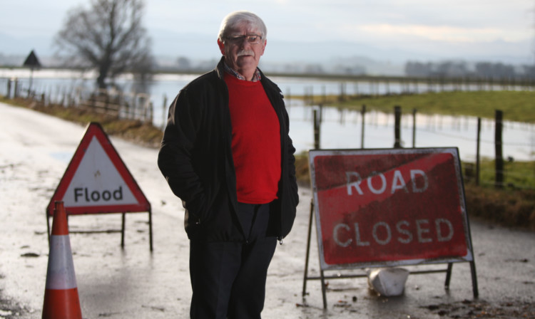 Councillor Melloy at the road closed signs, with areas of flooding behind.