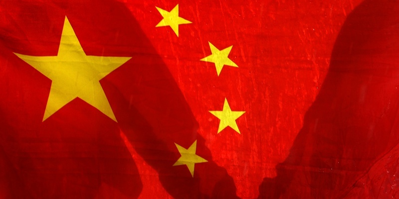 Two unknown people hold hands behind a Chines Flag