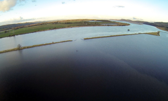 An aerial view showing the breach in the bank at Easter Rhynd, with the flooded fields in the foreground and the River Tay flowing towards Dundee in the distance.