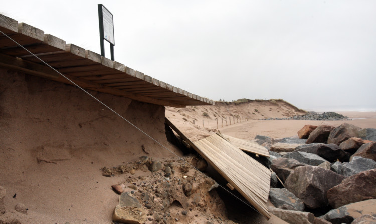 The damaged boardwalk with the dunes in the background.