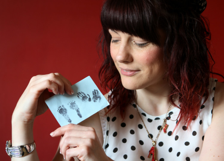 Paula Laurence holding a card with a reproduction of Bens foot and handprints.