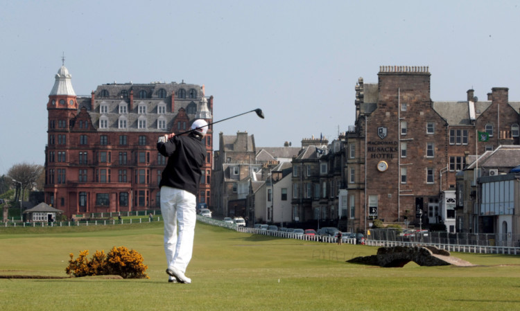 A golfer tees off on the 18th hole of the Old Course in St Andrews with Rusacks Hotel on the right.