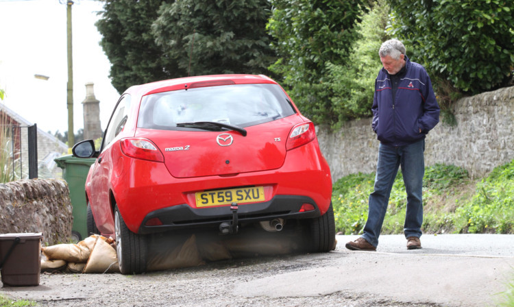 Bob Bell inspects the Mazda car which is perched on top of his sandbags.