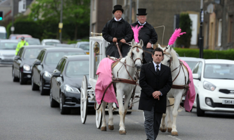 White horses dressed in pink lead the funeral cortege.