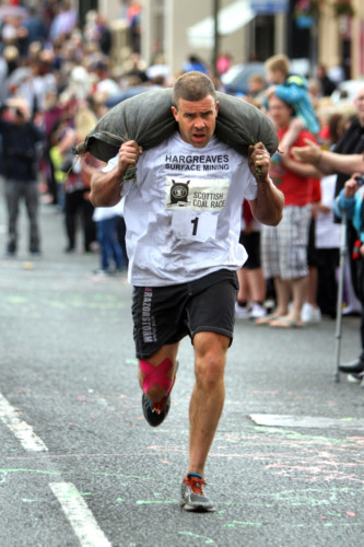 Kris Miller, Courier, 28/06/14. Picture today at Kelty Coal race shows competitors coming to the end of the 1km course carrying 50kg bags of coal for the men and 25kg bags for the women. Pic shows MENS WINNER, Graeme Crane.