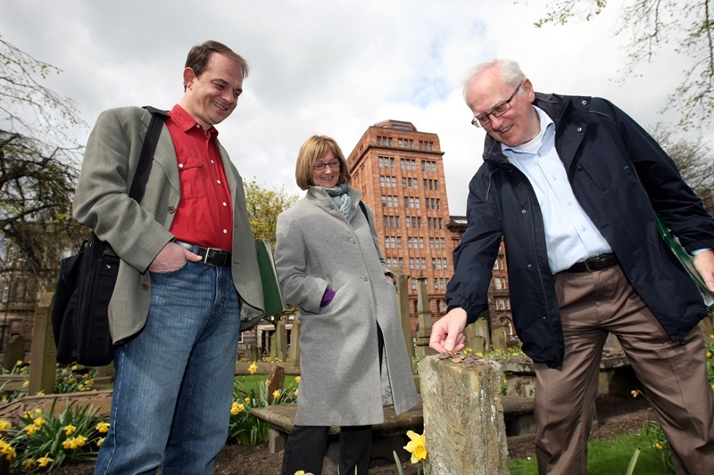 Steve MacDougall, Courier, The Howff, Meadowside, Dundee. Mystery surrounds the coins left on the Nine Trades stone marker. Pictured, left to right is Anthony Cox (tour guide with Tayside Heritage Tours), Frances Dobson and husband David Dobson. David has been tempted into leaving a coin on the stone, hopefully, for good luck.