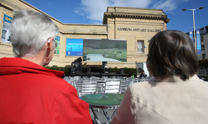 A couple watching the golf on the big screen in the fan zone beside the Concert Hall.
