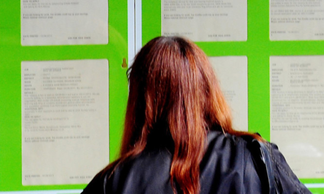 A woman searching for work in the window of a job centre.