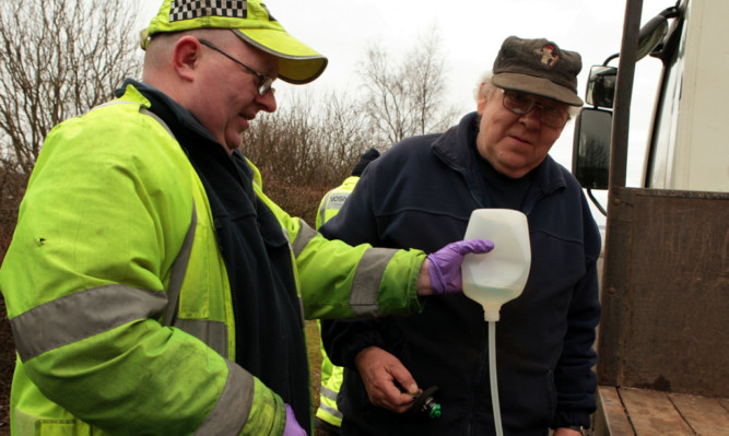 An excise officer checks the diesel in this motorist's tank for illegal fuel.