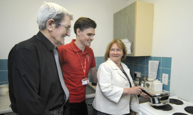 Minister for Public Health Maureen Watt visits Meal Makers and shows she can cook too, watched by Norman Quigg, left, the first recipient of the schemes help, and Meal Makers development officer Stuart Miller.