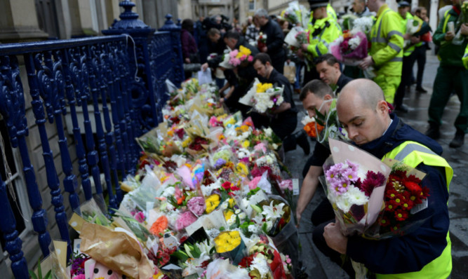 Emergency workers move flowers in Royal Exchange Square, Glasgow, Scotland, where the first victim was hit.