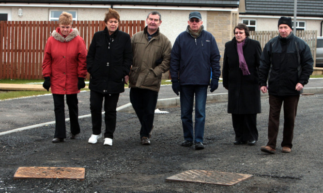 Boswell Knowe residents Wilma Florence, Avril Scott, Ian Florence, Ron and Mary McQueen, and Ian Brown beside some of the raised ironwork on the road that has never been properly surfaced.