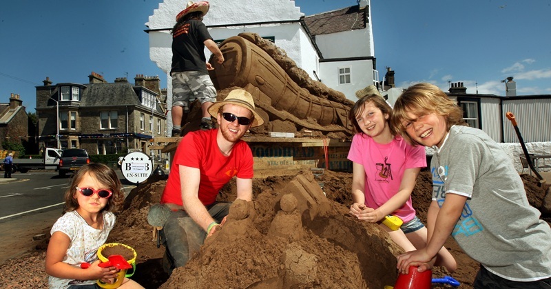 John Stevenson, Courier,02/07/10.Fife,Crail,East Neuk Festival.Pic shows Jamie Wardley of Sand In Your Eye, with his new 'apprentices' for the day holiday makers l/r Emily(6),Megan(12) and Sam(10) Jack, start their own sand sculpture in front of the giant steam engine being created by Jamies team.