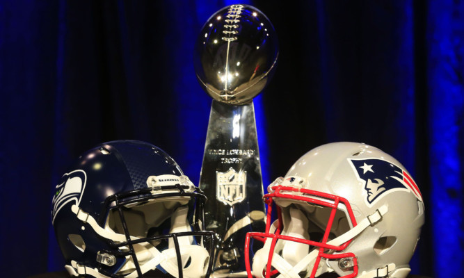 The Vince Lombardi Trophy is displayed between the helmets of the Seattle Seahawks (left) and New England Patriots.