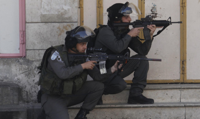 Israeli border police aim weapons toward Palestinian protesters in Hebron.