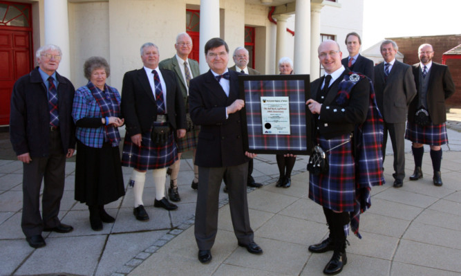 Steven Sim presents the framed registration document of the Bell Rock tartan to Roger Lockwood, chief executive of the Northern Lighthouse Board, with other invited guests looking on.