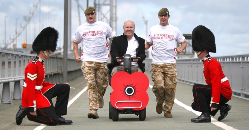 Kris Miller, Courier, 05/07/10, News. Picture today at Forth Road Bridge (South side). Veteran Andy Laker (on mobility scooter) is going to be crossing the Forth, Tay and Kincardine (please check with Dunfermline) bridges to raise money for Poppy Scotland. Pic shows Andy with members of the Scots Guard who will be offering support, Guardsman Michael Aitken (running left) and Lance Corporal Tam Taylor (running right).