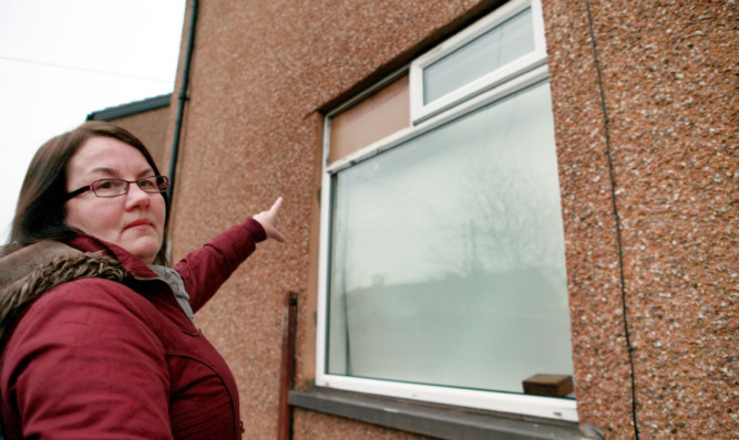 Irene Reilly points to the boarded up window broken by thieves.