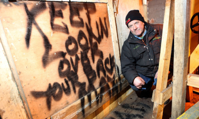 John Maxwell beside the threatening graffiti left by the thieves at his garage.